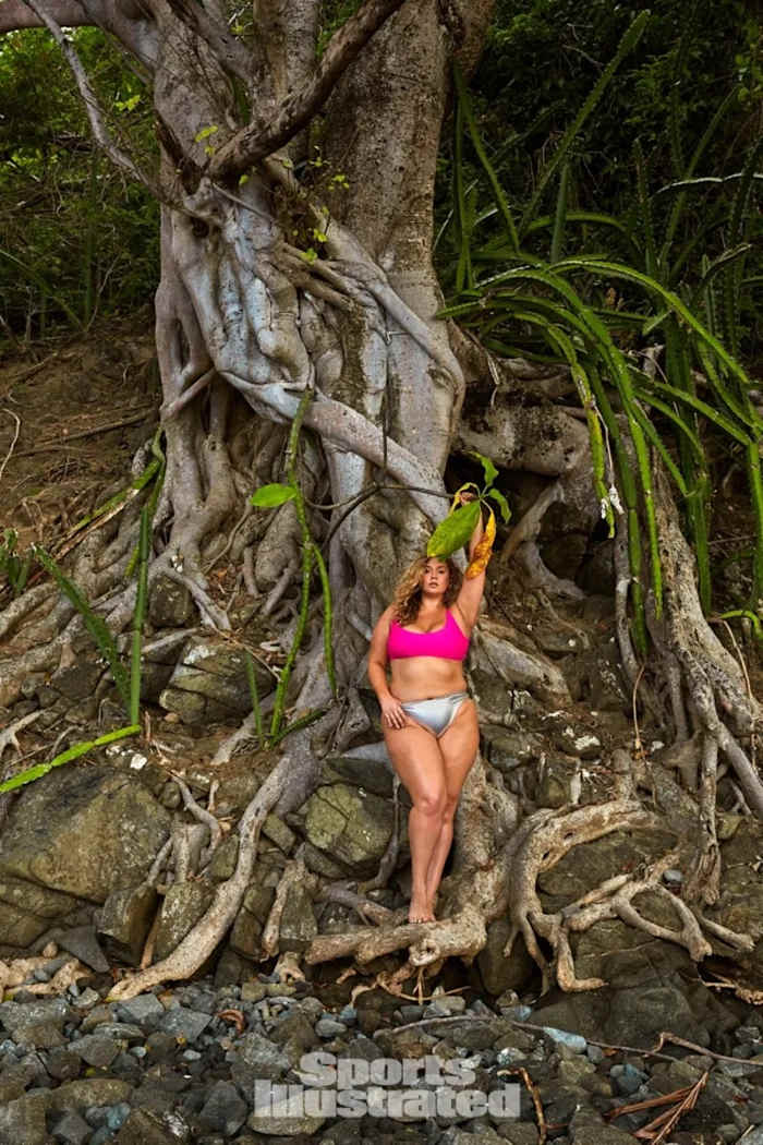 Hunter McGrady stands on the roots of a large tree in a hot bikini bikini top and metallic bikini bottoms.